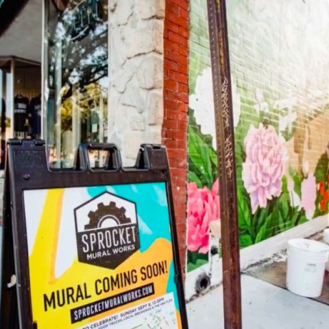 A street sign advertising Sprocket Mural Works next to a mural in progress.